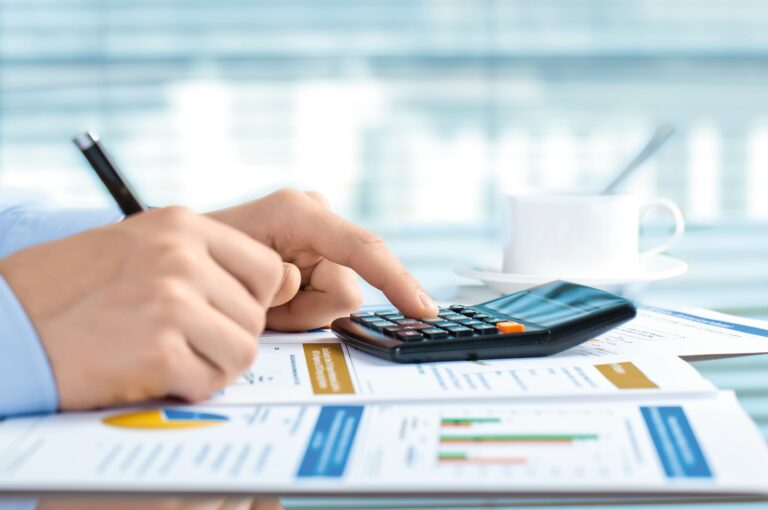 Person uses a calculator and analyzes diagrams and statistics on a business report, a coffee cup in the background.