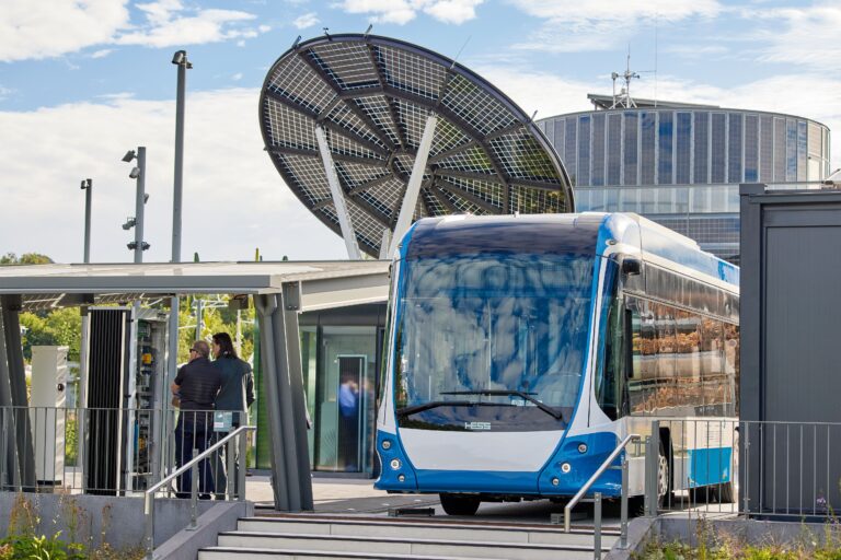 Elektrobus im AES-Ladepark vor einer blütenförmigen Solaranlage und moderner Gebäudearchitektur – zukunftsweisende Ladeinfrastruktur für den öffentlichen Nahverkehr.
