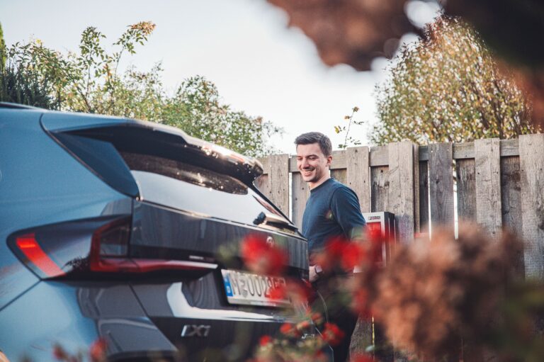 Man charging his electric car (BMW iX1) with a wallbox in the garden - relaxed scene in daylight with autumnal surroundings.
