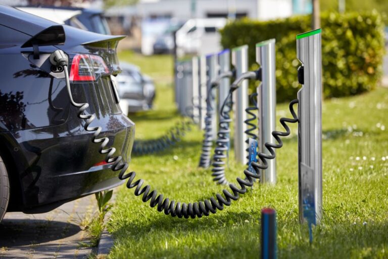 Elektroauto wird auf einer begrünten Parkfläche über eine spiralförmige Ladekabelverbindung mit einer Reihe moderner Ladesäulen aufgeladen