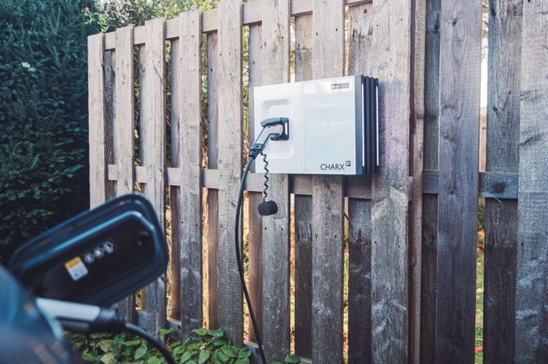 Auto lädt mit AC-ladekabel an privater Wallbox zu Hause, die an einem Zaun befestigt ist.