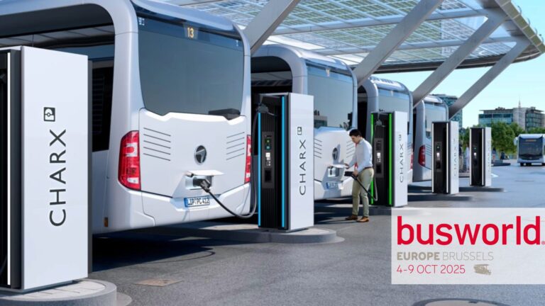 A row of electric buses is being charged at CHARX charging stations. A person is connecting one of the buses to a station. In the background, a modern bus terminal with solar panels on the roof is visible. Text in the image reads: ‘busworld EUROPE BRUSSELS 4–9 OCT 2025.