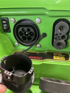 Nahaufnahme eines Ladeanschlusses für Elektrofahrzeuge auf einer grünen Fläche.