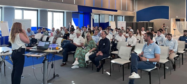 Raum mit mehreren Personen die bei einem Vortrag zuhören.