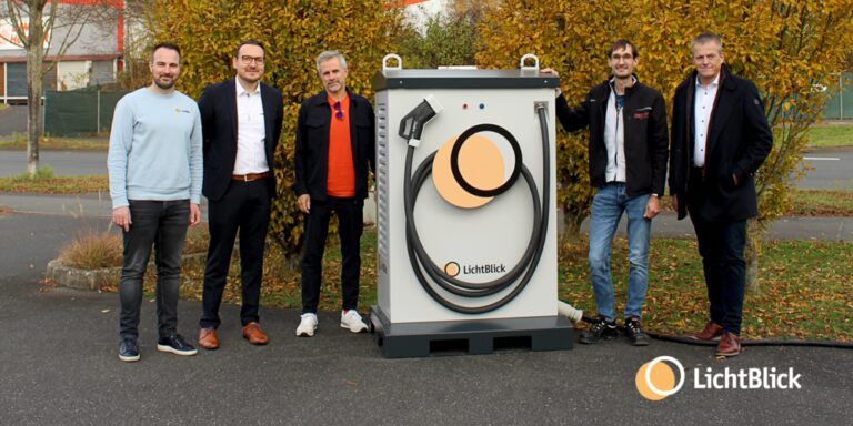 In der Mitte des Bildes ist die mobile Ladelösung FlexiCharge Pro von LichtBlick zu sehen. Links neben der mobilen Ladelösung stehen drei Herren. Recht von der Ladelösung stehen zwei Herren.